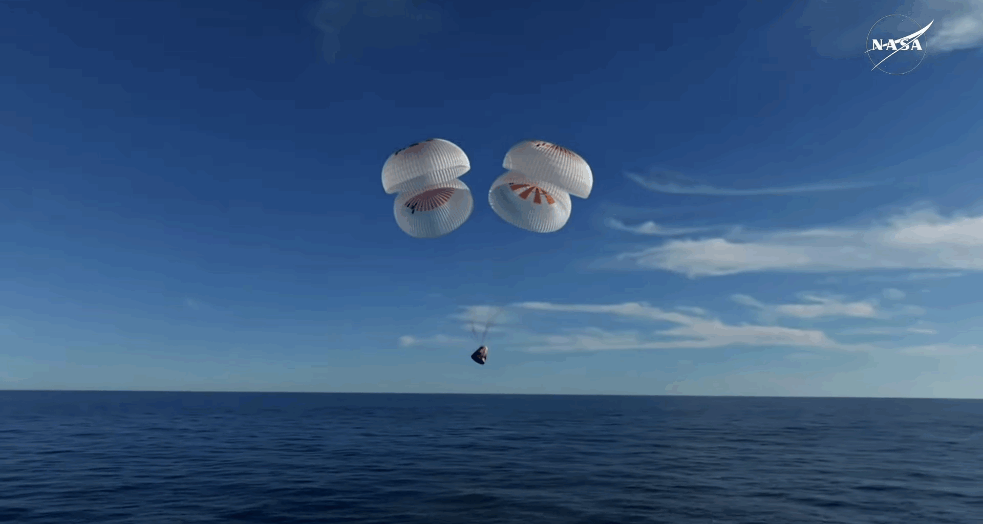 a white space capsule descends toward the ocean under four white and red parachutes