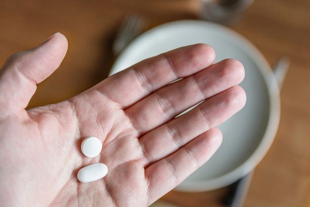 Close-up view of a white male hand holding two white pills in the palm of hand