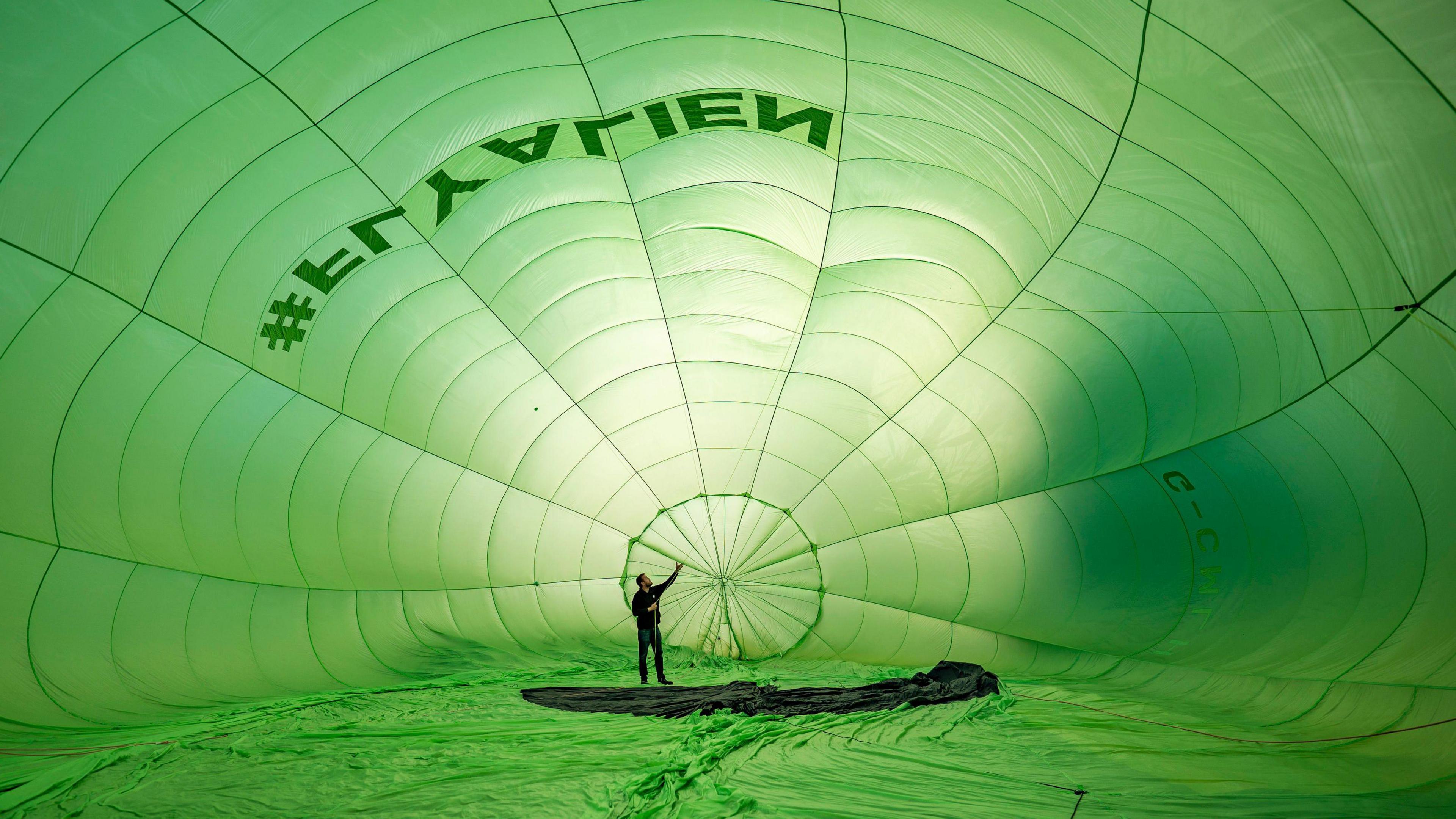 A man is standing in a giant green balloon as it inflates 