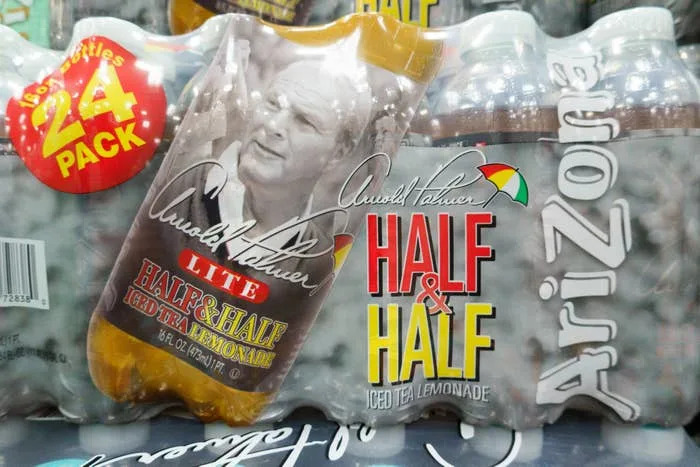 Cans of Arizona Arnold Palmer Lite Half & Half, a mix of iced tea and lemonade, in a 24-pack with Arnold Palmer’s signature and image visible on packaging