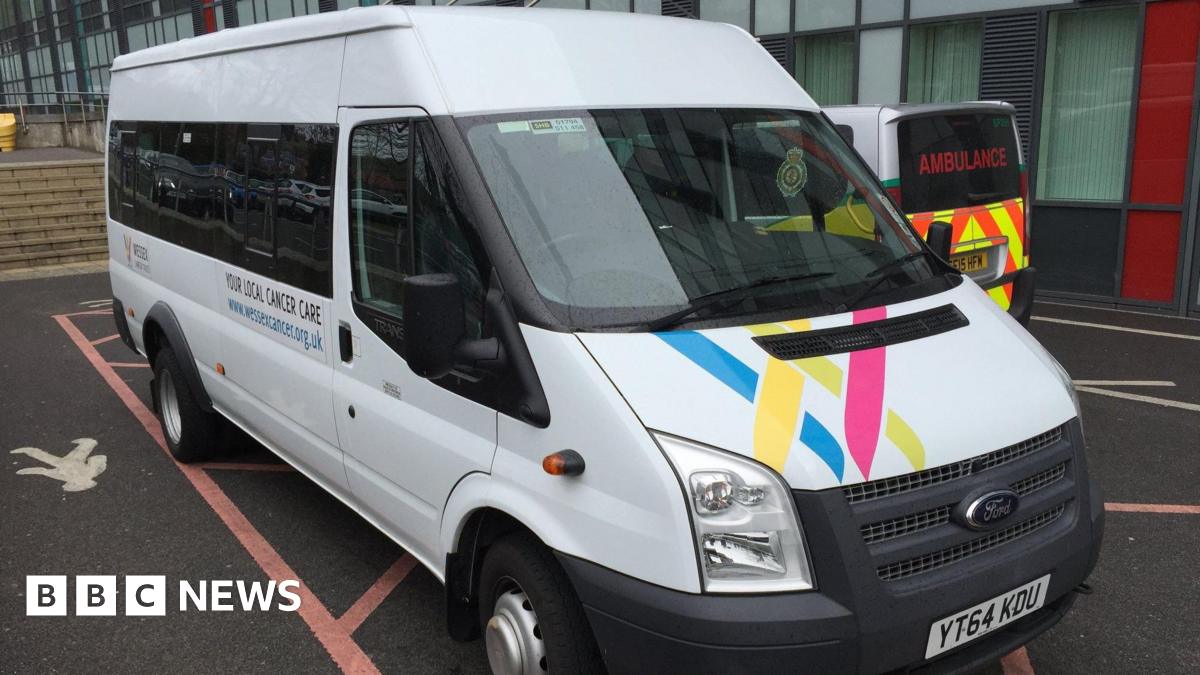 A white Ford Transit minibus with Wessex Cancer Support branding parked outside a hospital, with an ambulance beside it.