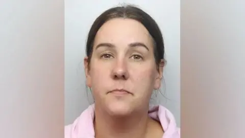 Northamptonshire Police A police mugshot of Lucy Connolly. She is staring directly down the camera, with a neutral expression. Her hair is pulled back over her ears and behind her, in what appears to be a ponytail. She is wearing a pink top. 