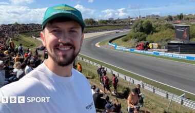 Brandon Burgess smiles while taking a selfie with the Zandvoort circuit in the background