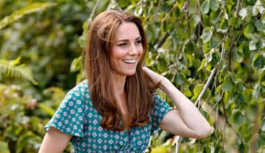 Kate Middleton smiling as she stands outdoors near some trees and plants