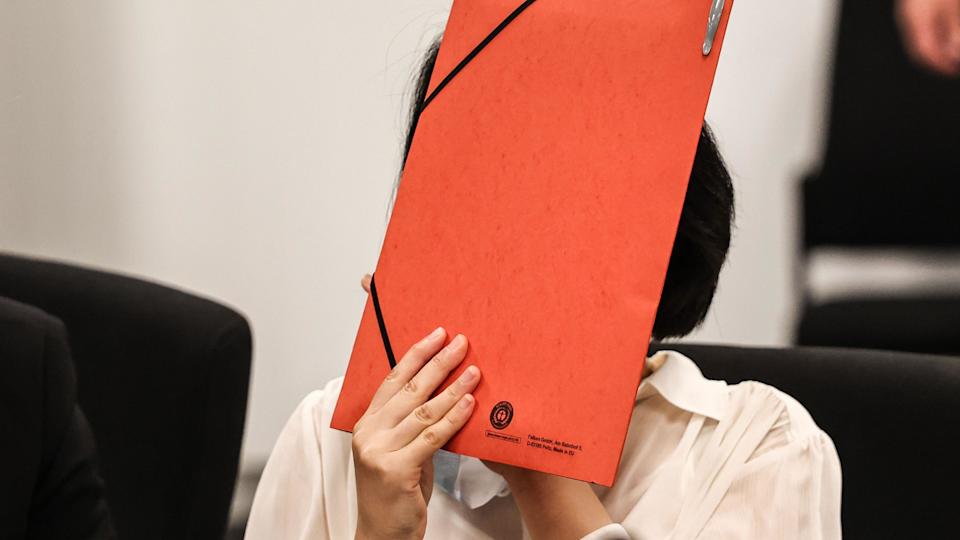A woman in a white shirt holds a red folder in front of her face