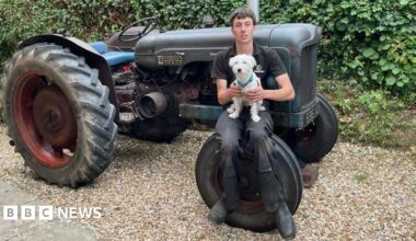 Billy Kitcher sat on his tractor's front tyre holding his small white dog.