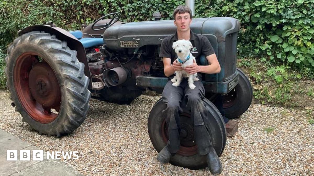 Billy Kitcher sat on his tractor's front tyre holding his small white dog.
