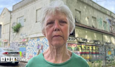 Ann Devereaux stands beside the derelict property next door - a large building now overtaken by decay. Graffiti covers the walls, weeds and shrubs grow unchecked from cracks in the brickwork, and gaping holes expose the interior to the elements.