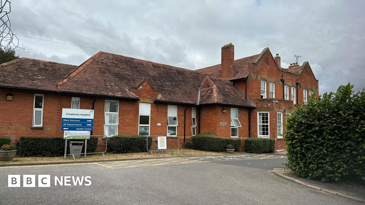 A red brick cottage hospital building in Crewkerne with red tiles roof and white sash windows and a single storey extension with hedges outside