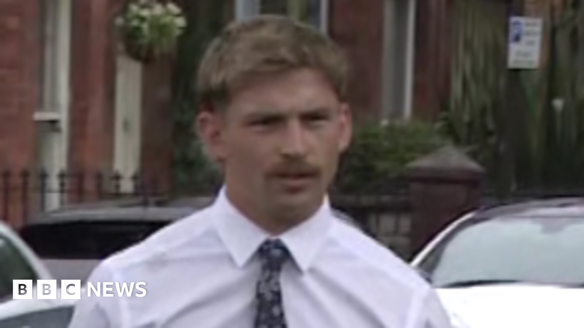 Kavan Keenan is a young man with short blonde/ brown hair and a moustache. He is walking towards the gates into the court as the picture is taken. He is wearing a white long sleeve shirt and a black patterned tie. Behind him is a silver car and two white cars parked along the street in front of red brick terrace houses.