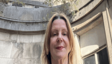 Maria Kane pictured standing outside of an old building at the Bristol Royal Infirmary. She has short blonde hair and is wearing a green leopard print dress. She is looking down at the camera