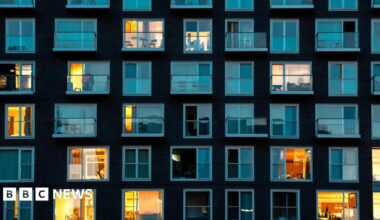 Stock image of a modern building facade in London at night - it shows residential flats where there are five rows of windows in the shot, some with curtains closed and lights off and some with lights on.