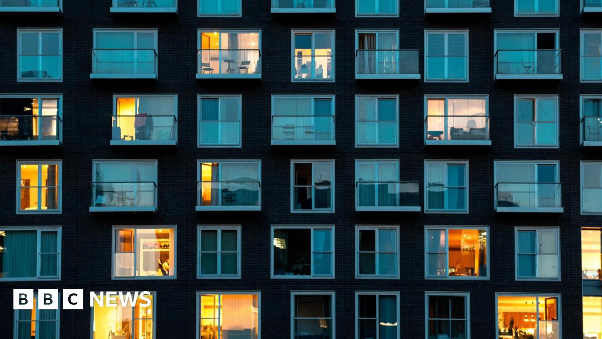 Stock image of a modern building facade in London at night - it shows residential flats where there are five rows of windows in the shot, some with curtains closed and lights off and some with lights on.