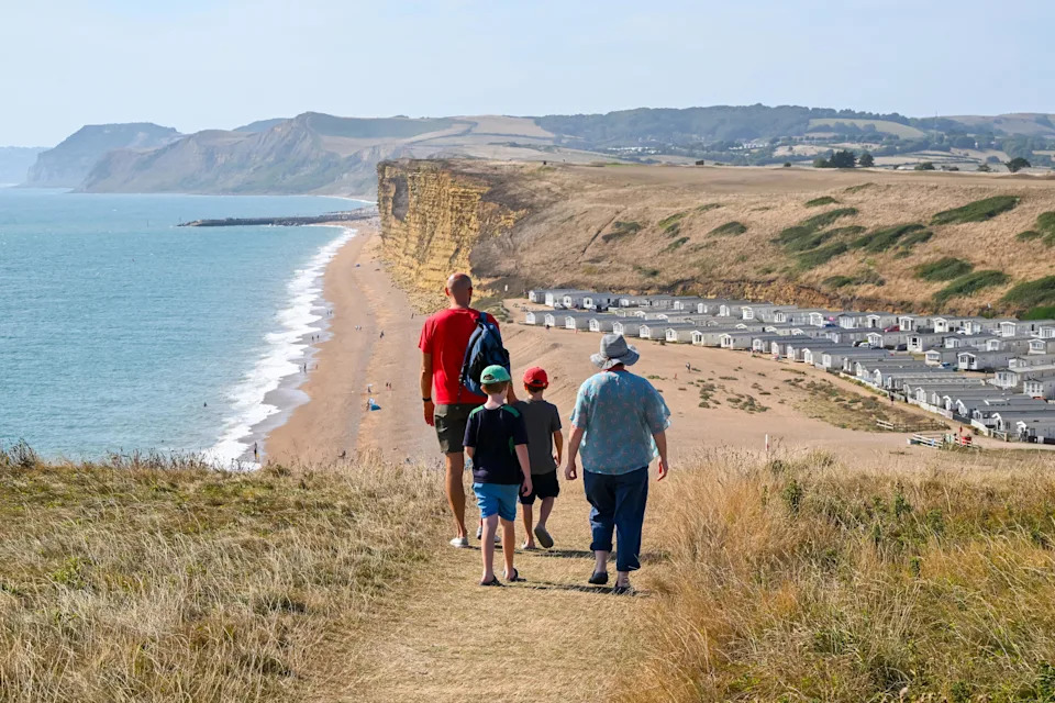Burton Bradstock, Dorset, UK.  17th August 2025.  UK Weather.  Walkers on the South West Coast Path take in the view of the drought scorched coastline as they walk towards Freshwater Beach Holiday Park at Burton Bradstock on the Dorset Jurassic Coast on a scorching hot afternoon as the heatwave continues during the summer holidays.   Picture Credit: Graham Hunt/Alamy Live News