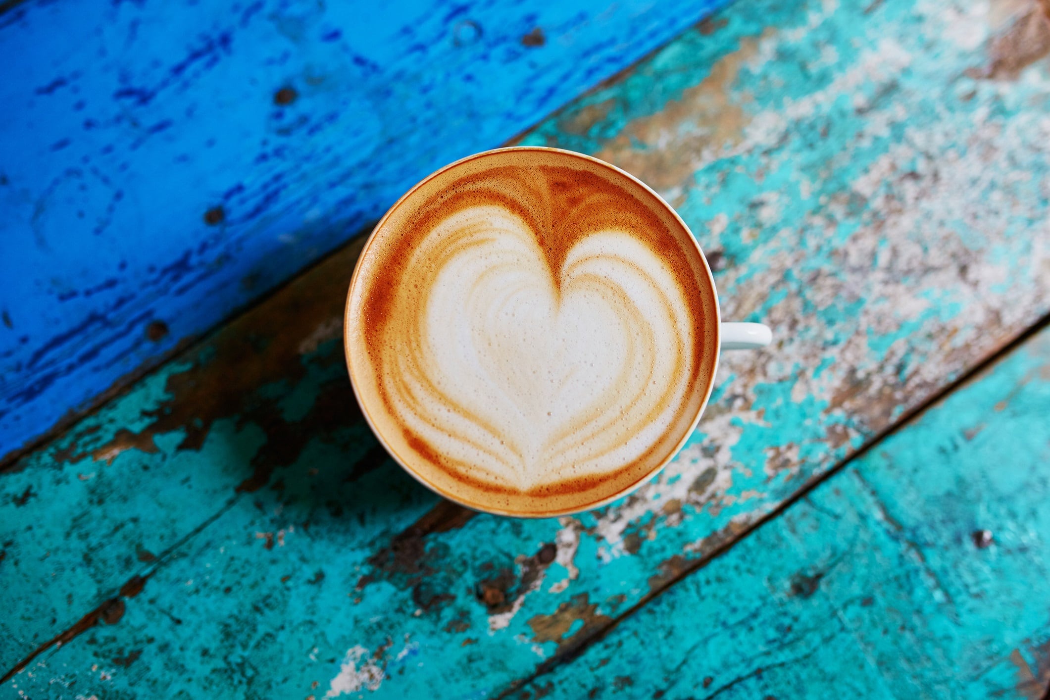 Cup of fresh coffee with heart form milk drawing on blue wooden table, view from above, flat lay.
