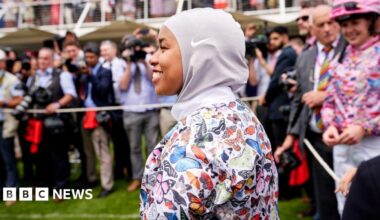 A female jockey wearing a hijab and top with colourful butterflies on it.