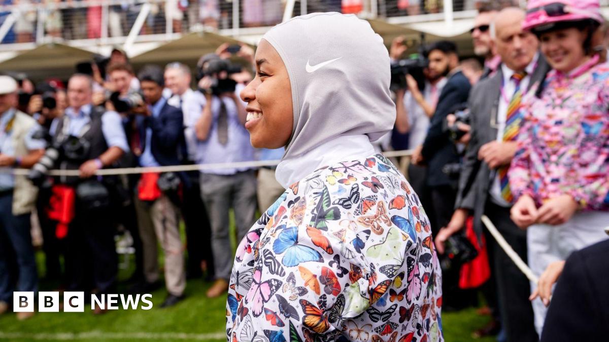 A female jockey wearing a hijab and top with colourful butterflies on it.