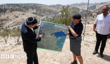 Israeli Finance Minister Bezalel Smotrich (L) helps to hold up a map showing the plans for the E1 settlement project during a visit to the area, in the occupied West Bank, on 14 August 2025