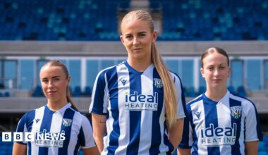 Three female football players stand in blue and white West Bromwich Albion kits in a football stadium.