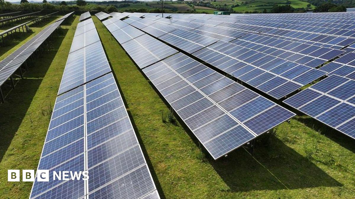 Stock image of a solar farm, with glass panels facing the sky and placed on fields in the countryside