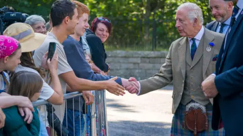 PA Media King Charles III meets members of the public after inspecting the Balaklava Company, 5th Battalion, The Royal Regiment of Scotland, at the gates of Balmoral, who are standing behind a metal barrier.