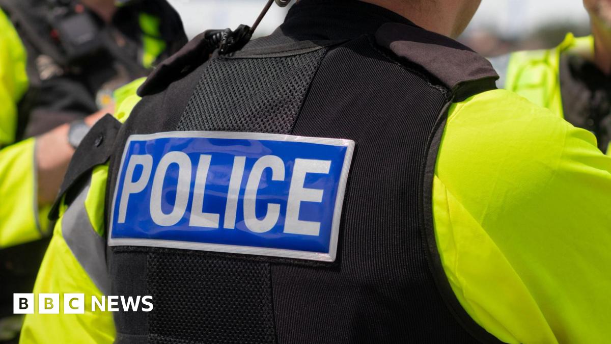 The back of a police officer. They are wearing a yellow high-vis jacket and a black vest with the word 'police' across the back.