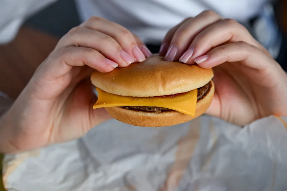 PRODUCTION - 09 September 2024, Berlin: A woman holds a cheeseburger in her hands at the opening event of the McDonalds branch in Alboinstraße. The M consists of two juicy patties made from beef from Germany and a creamy special sauce. Photo: Jens Kalaene/dpa (Photo by Jens Kalaene/picture alliance via Getty Images)