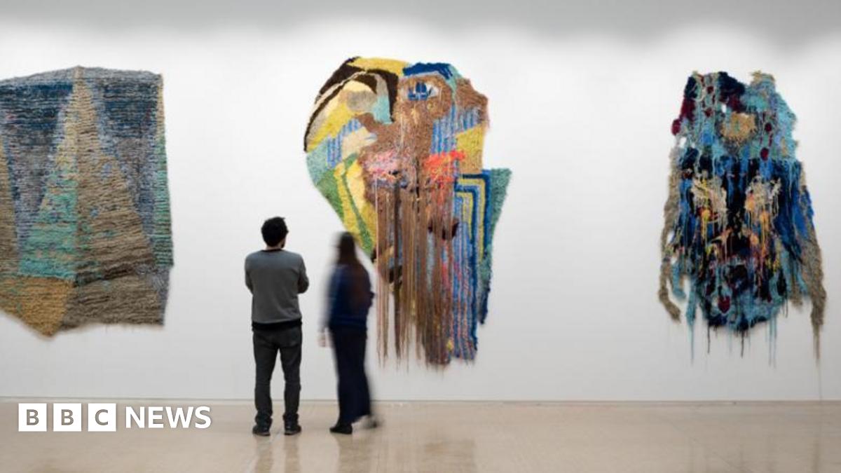 A photo of two people looking at artwork on a wall, which looks like a smear of coloured paint.