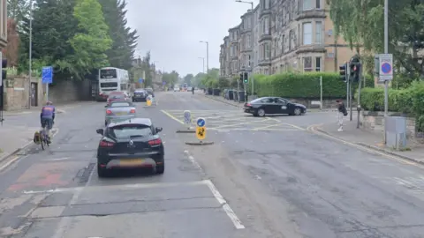 Google Dalkeith Road has a line of cars and a bus travelling along it at a crossroads.