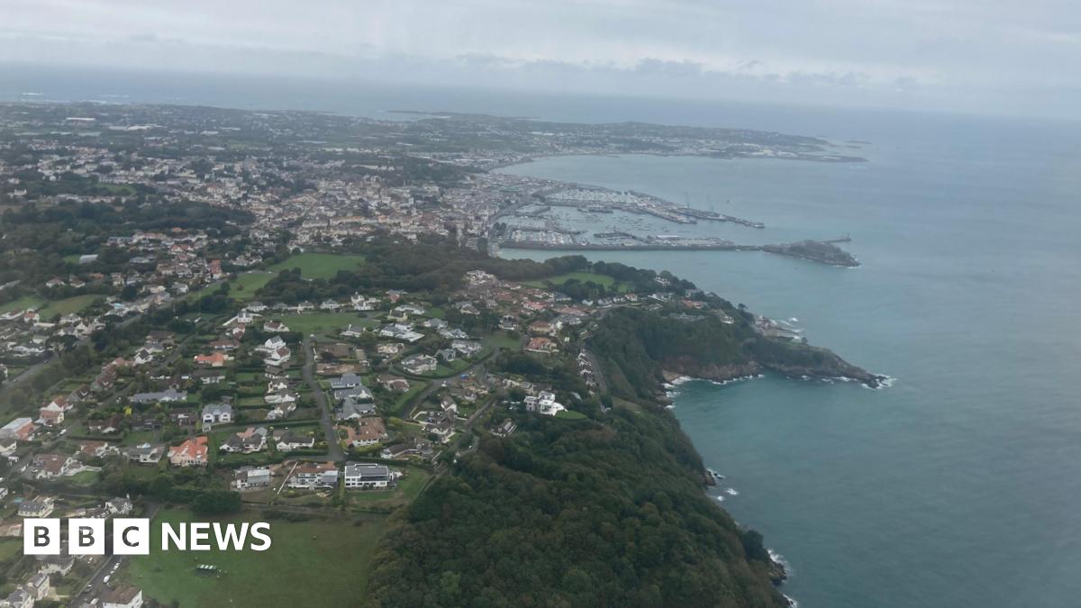 Arial view of Guernsey. The sea is a dark blue and the sky is grey and full of clouds.