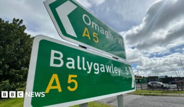 Two green road signs, one reading Omagh A5 and the other reading Ballygawley A5. There is a cloudy sky above.