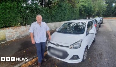 A man stands by a white parked car
