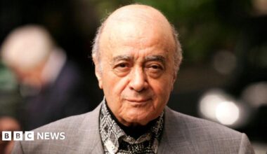 Mohamed Al Fayed in a grey suit with out of focus lights behind him