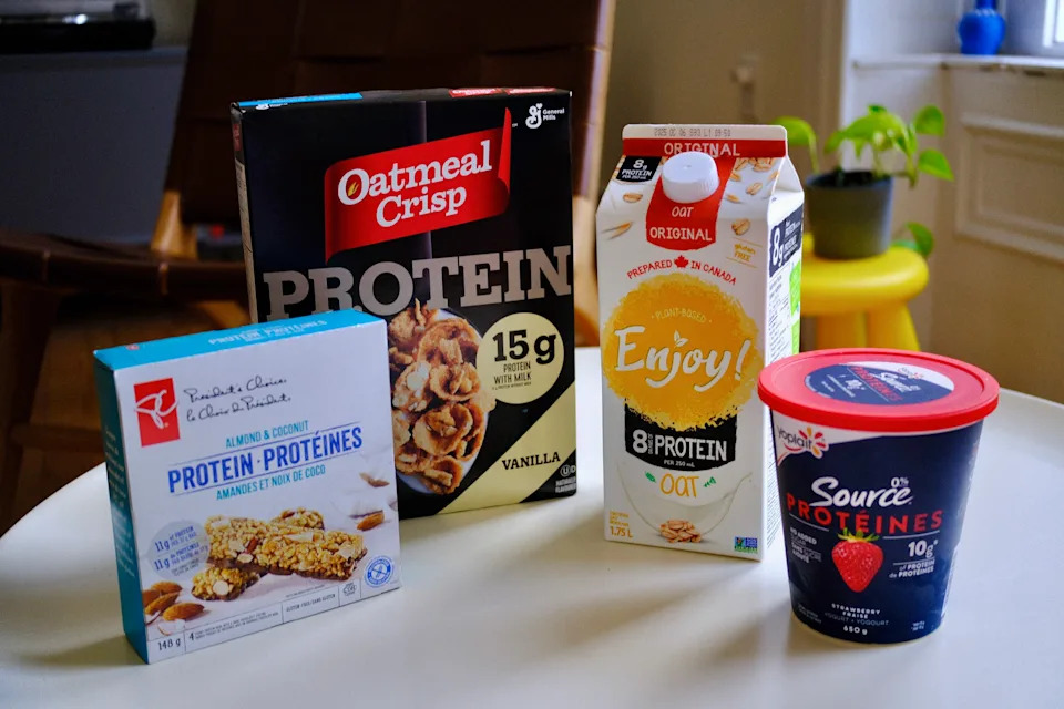 Granola bars, cereal, milk and yogurt sit on a white table lined up, all of which feature protein as an ingredient. (Photo: Chris Stoodley/Yahoo Canada)