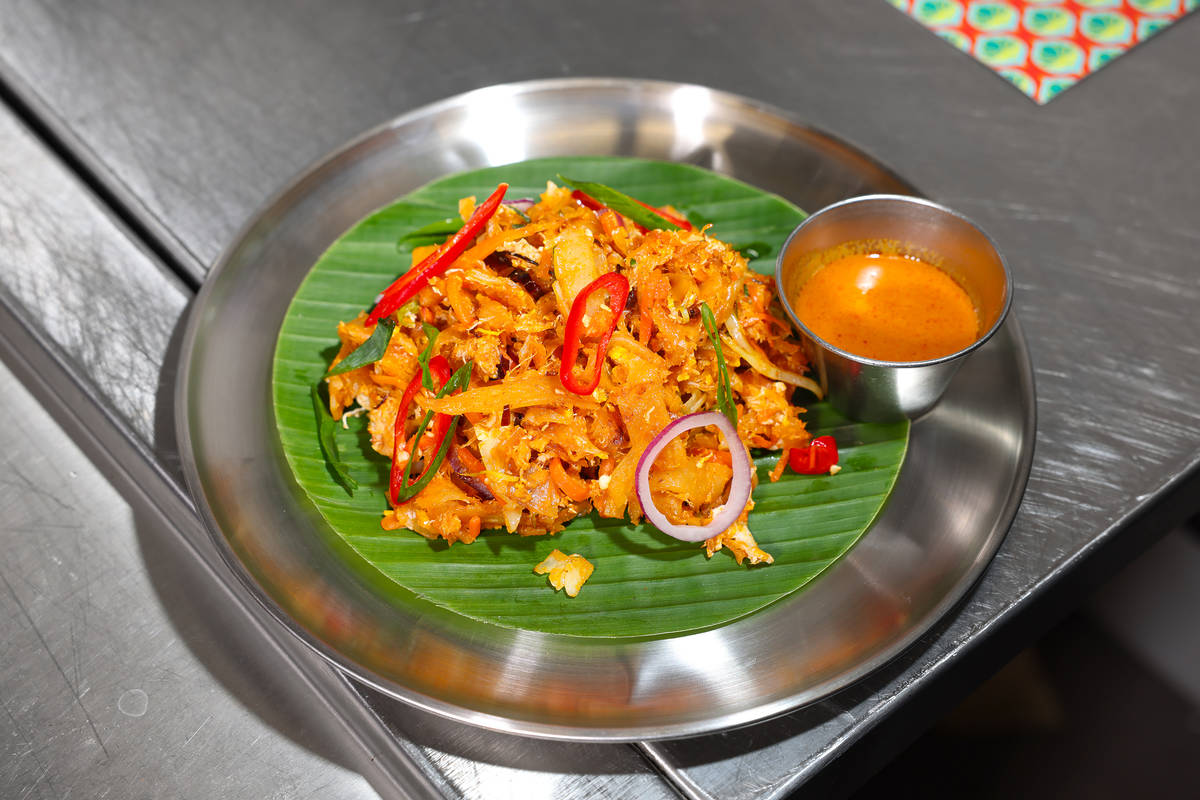 a metal plate with a dish of kothu on top - shredded roti stirfried in curry sauce