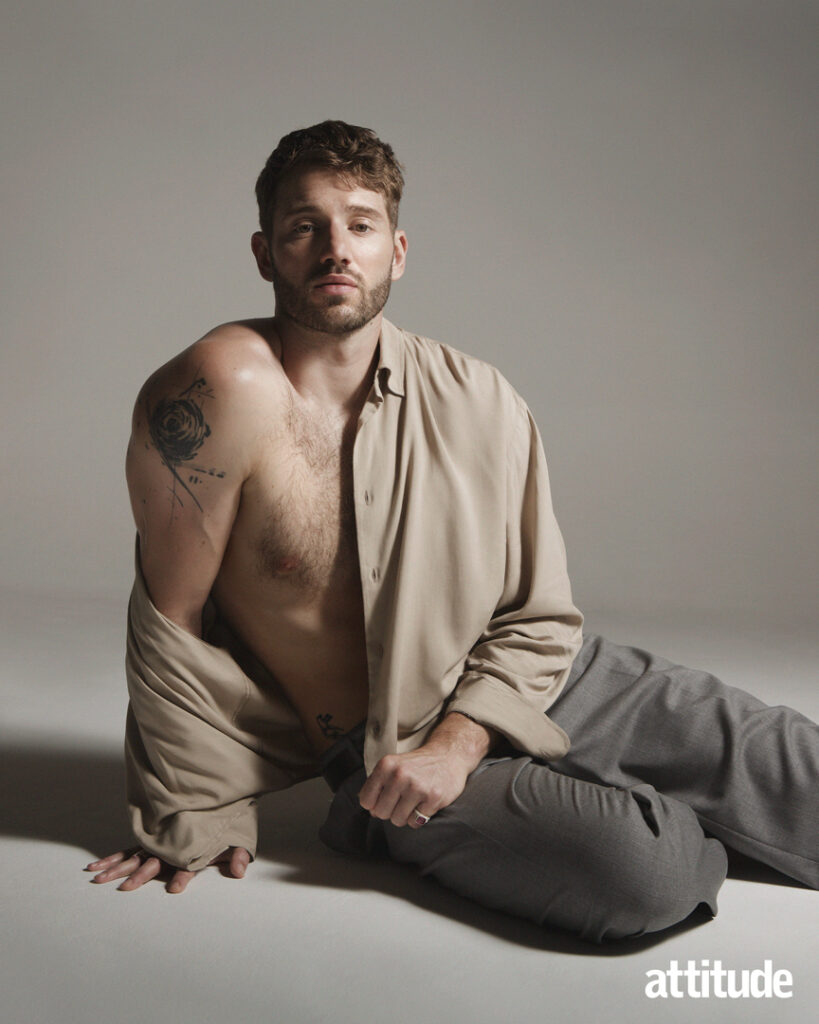 Alex kneeling on the ground in a beige shirt with one shoulder exposed