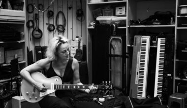 Black and white photo of Biz Lyon playing guitar, in a music room