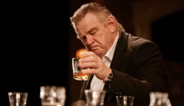 Brendan Gleeson as Jack examines a whiskey glass at the bar in The Weir, surrounded by pints and spirits.