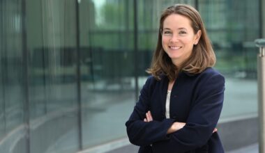 Dana Orange stands in a black coat before a glass wall