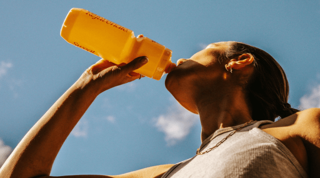 Female drinks out of orange bottle, with blue sky above