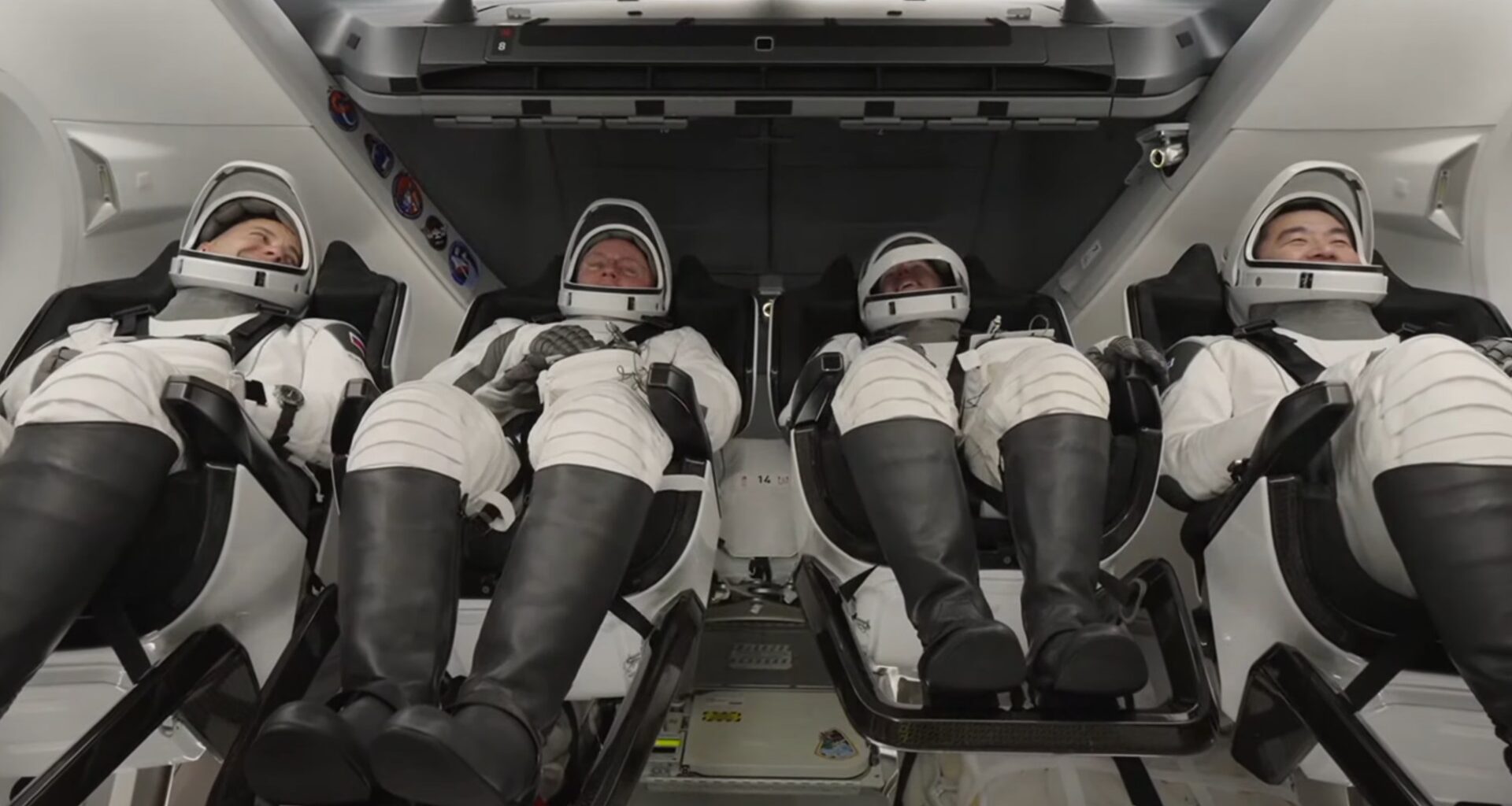 four astronauts in white spacesuit recline inside a white spacecraft cabin