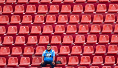 A fan sits alone in a stand at a stadium with rows of empty red seats all around him