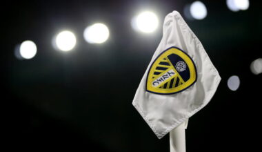 A corner flag with the Leeds United badge on it is seen in the dark with floodlights in the background