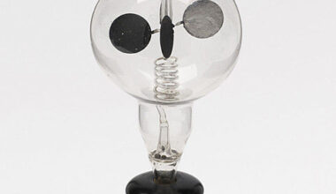 Image of a wooden stand holding a sealed glass bulb with a spinning set of vanes, each of which has a lit and dark side.