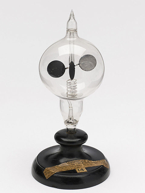 Image of a wooden stand holding a sealed glass bulb with a spinning set of vanes, each of which has a lit and dark side.