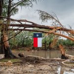 CENTER POINT, TEXAS - JULY 13: A Texas flag hangs from a storm-damaged tree on the banks of the Guadalupe River on July 13, 2025 in Center Point, Texas. More than 160 people are still missing after storm cells halted over the area, dumping nearly 15 inches of rain and causing a 22-foot rise along the Guadalupe River. (Photo by Brandon Bell/Getty Images)