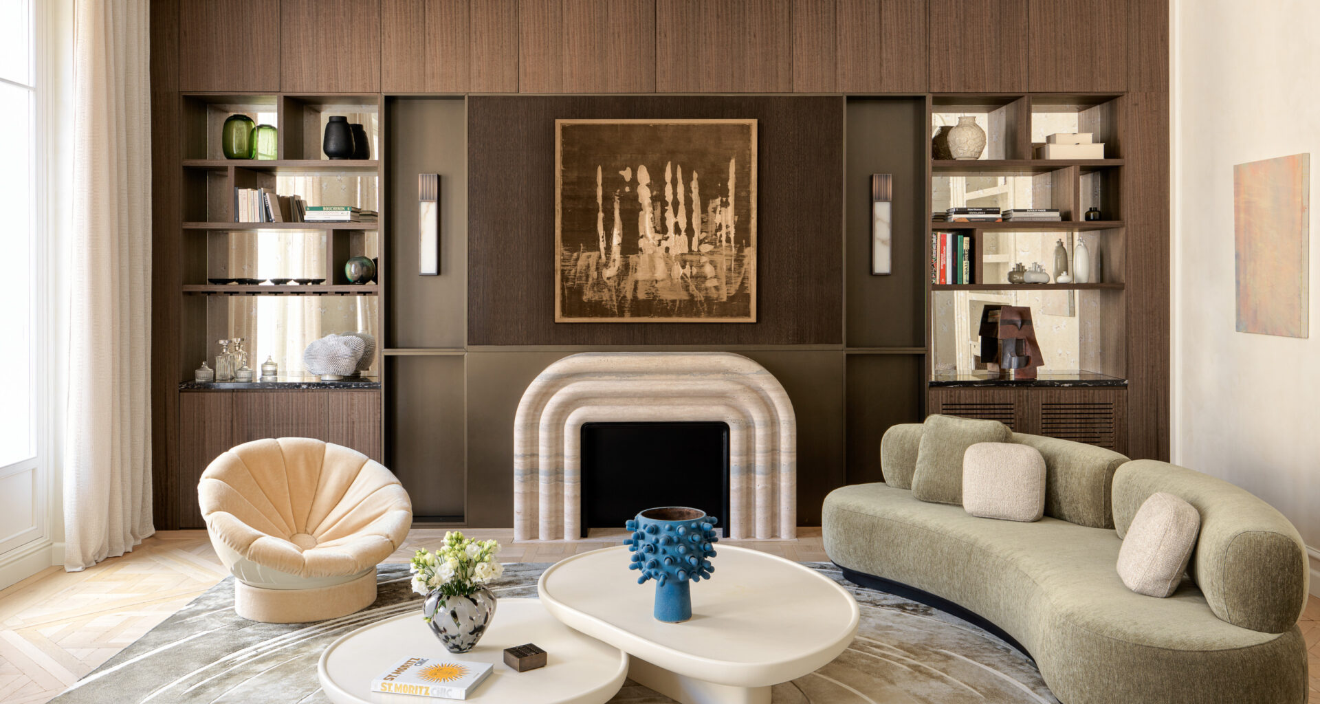 Cream living room with dark wood joinery, curved fireplace, sage green curved sofa, white nested coffee tables and peach chair
