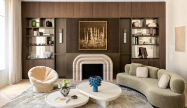 Cream living room with dark wood joinery, curved fireplace, sage green curved sofa, white nested coffee tables and peach chair