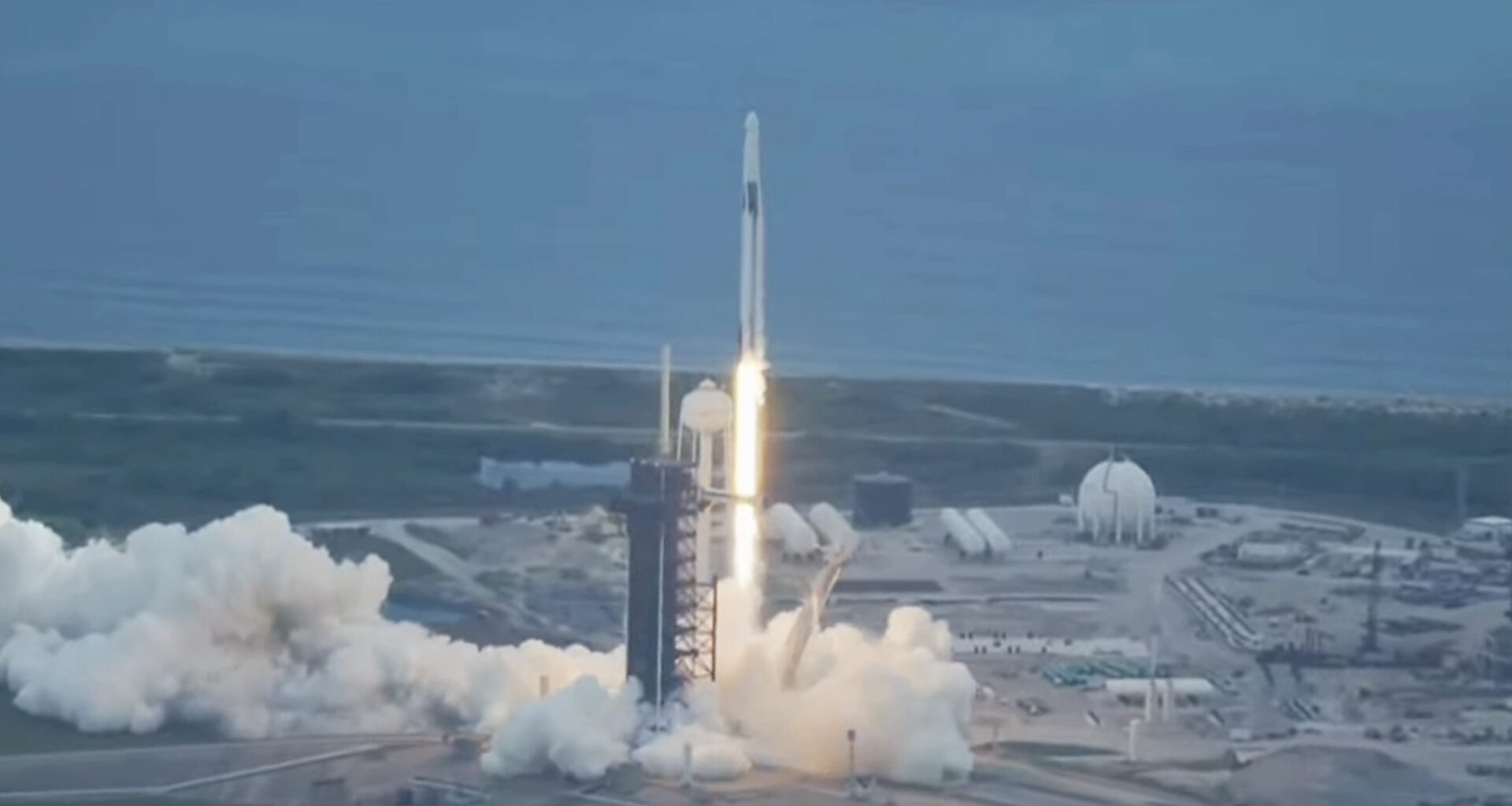A rocket seen shooting upward with a coastline in the background.