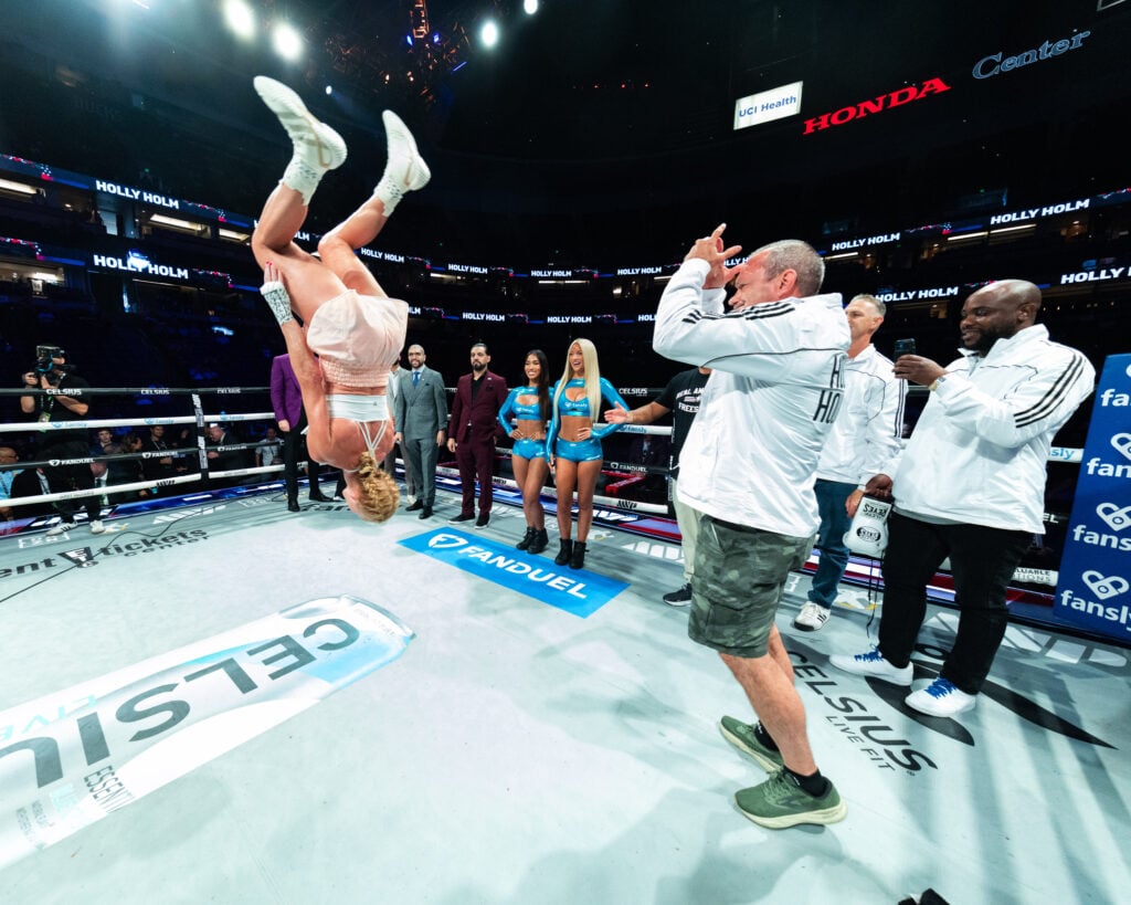 Holly Holm's coaches watch as she performs a back flip following her win